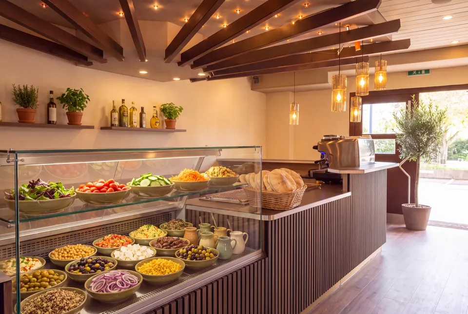 Salatbuffet in der Vitrine an der Lamellentheke: Blattsalate, Tomaten, Gurken, Couscous, Kichererbsen, Feta, Oliven und Dressings (Symbolbild auf Basis einer Aufnahme des Lokals)